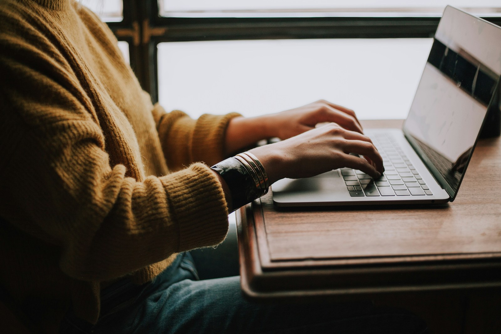 Persona navegando cómodamente una página web profesional y moderna en notebook, dentro de un entorno elegante con tonos neutros cálidos