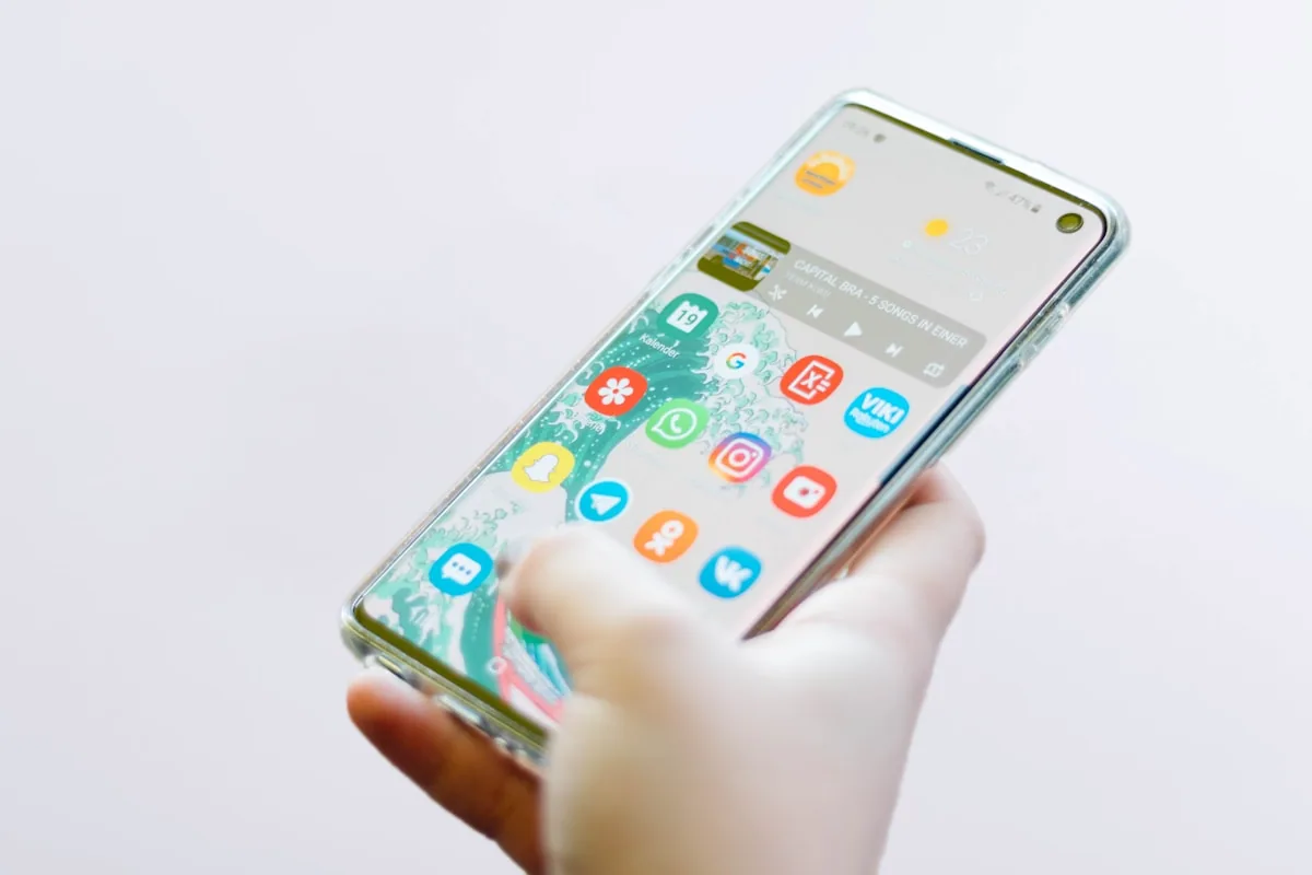 Mano sosteniendo un smartphone con pantalla de aplicaciones coloridas, múltiples íconos y notificaciones representando la saturación digital