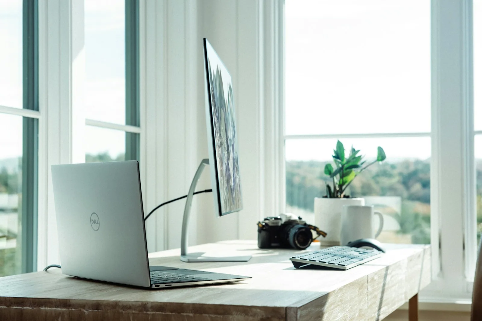 Escritorio profesional minimalista con laptop y monitor frente a una ventana luminosa, espacio de trabajo moderno