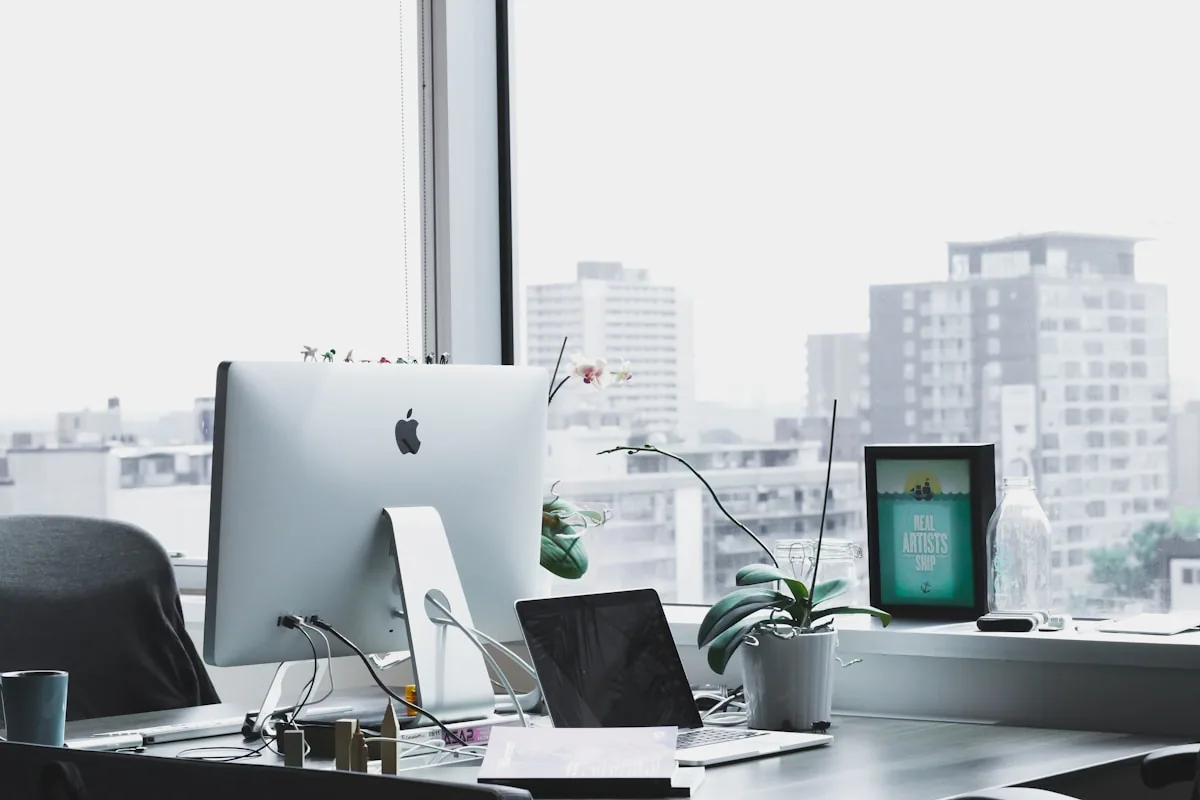 Workspace profesional con iMac y MacBook en una oficina con vista a la ciudad, entorno moderno y contemporáneo