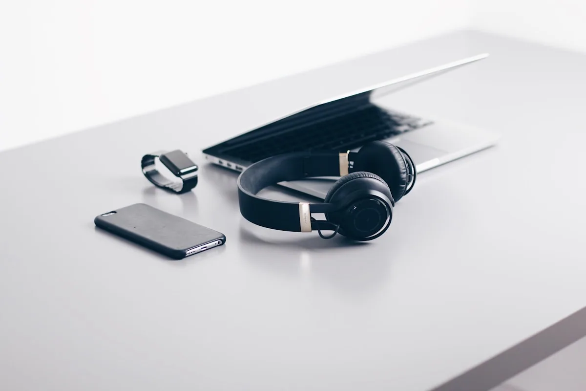Laptop, smartphone y auriculares sobre una superficie blanca representando el ecosistema multi-dispositivo de un profesional moderno