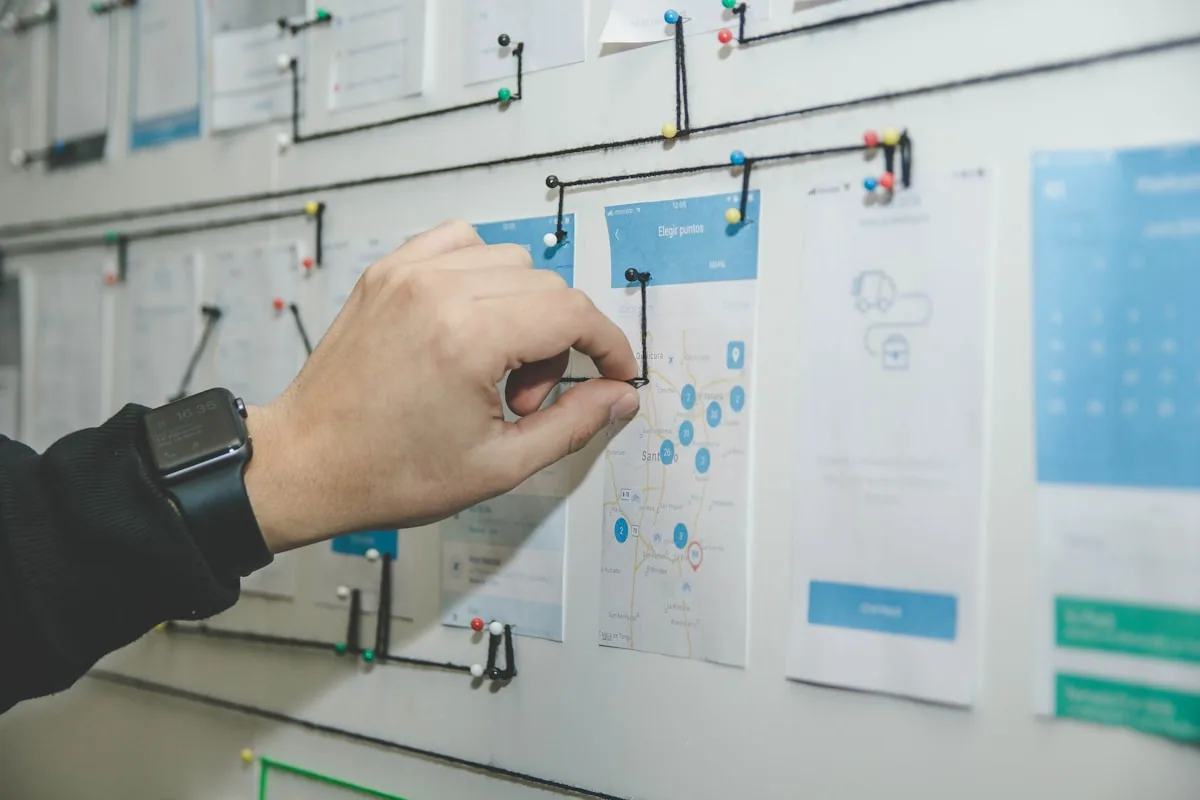 Mano organizando wireframes y flujos de usuario en un tablero de planificación con pins de colores, proceso de diseño UX